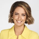 Brooke Boney is looking and smiling directly at the camera with a plain white background. She is wearing a yellow, collared top.