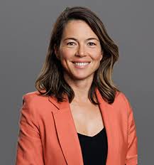 Alison Roberts is wearing a black top and a salmon pink blazer, smiling at the camera.